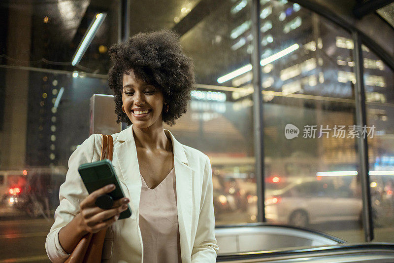 在圣保罗大道地铁站，一名手持智能手机的女子的肖像，São Paulo，巴西。每天通勤上班。